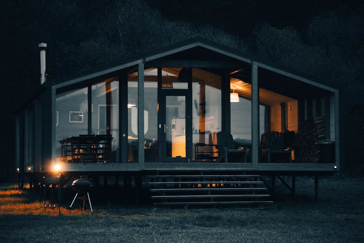 A modern glass fronted cottage glowing warmly at dusk
