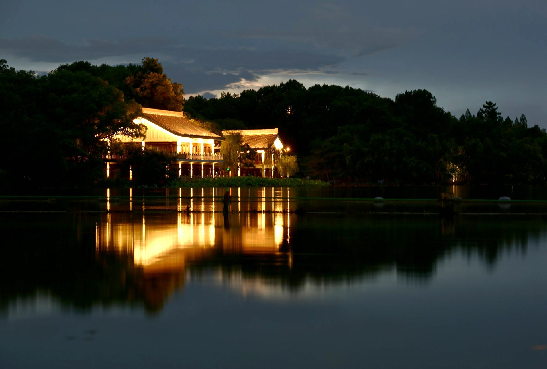 A lakeside cottage glowing warmly at dusk, reflected in still water
